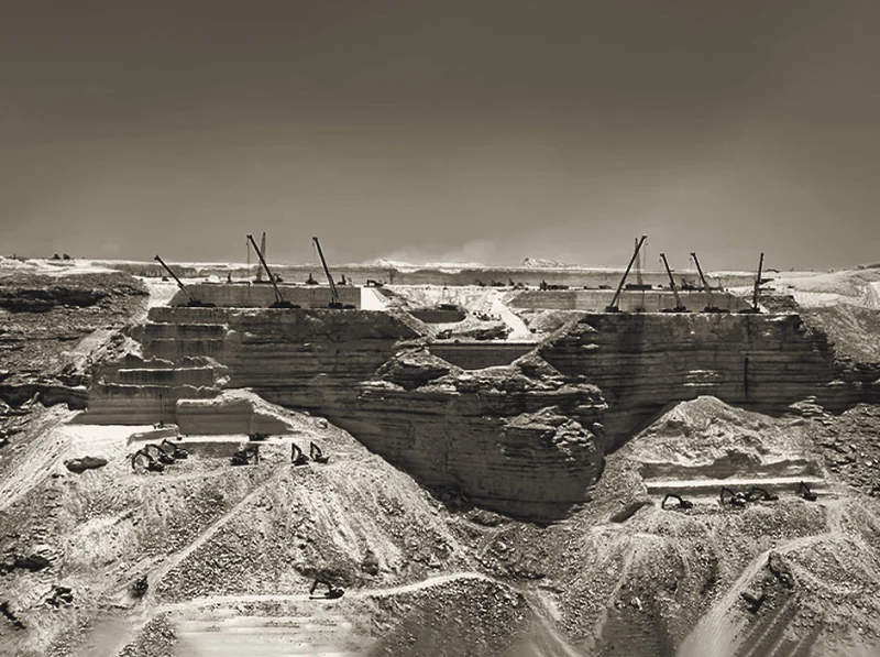 Excavated stadium bowl with earthworks plant and tower cranes on a desert site.